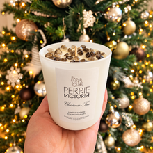 Load image into Gallery viewer, Hand holding a white Perrie Victoria Christmas Tree candle topped with smoky quartz crystals in front of a decorated Christmas tree.
